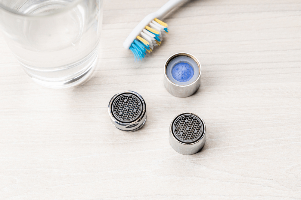 Using a small brush to remove debris in the faucet aerator